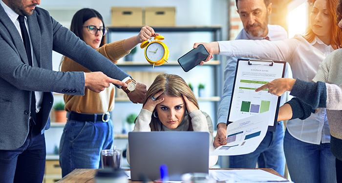 Businesswoman at laptop feeling crazy busy with coworkers hovering over her