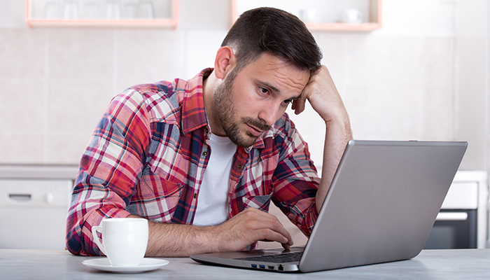 Bored man looking at laptop from home kitchen table