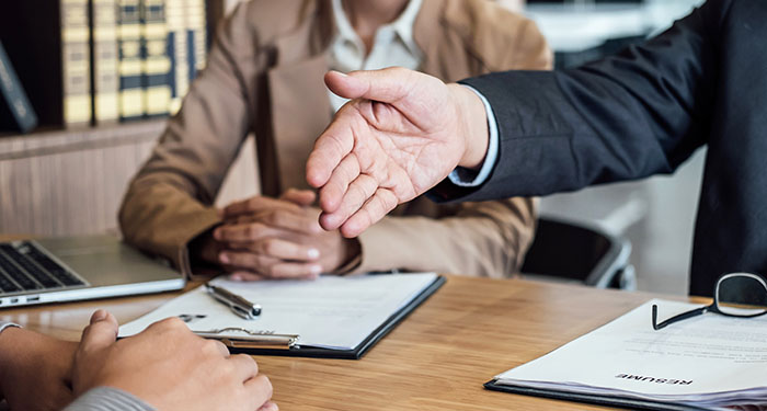 Three business people and one reaching hand out to shake on a promotion.